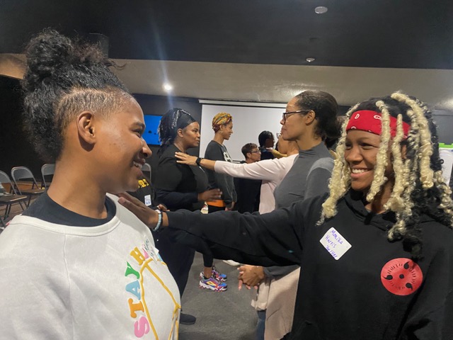 Black women practicing empowerment self-defense techniques, smiling and engaging in verbal and physical exercises. This is an example of one of our Own Your Own Safety workshops.