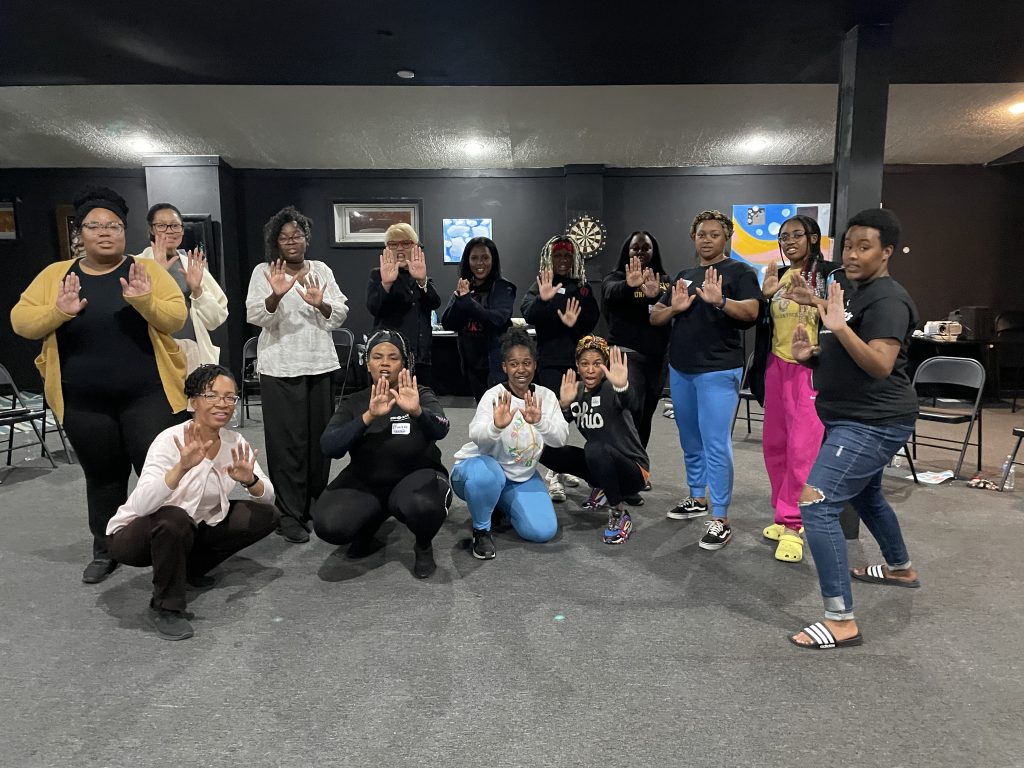 Black women graduates of an empowerment self-defense program, posing with raised hands in a Stop Sign gesture, symbolizing setting boundaries.